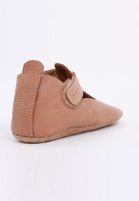 Miękkie brązowe skórzane buty dla niemowląt z szytą podeszwą i regulowanym paskiem, ustawione pod kątem, aby pokazać szczegóły z tyłu i boku na białym tle.
