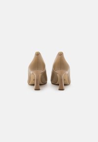 Chaussures à talons hauts en cuir nude avec une finition lisse, dotées d'une pointe arrondie et d'un talon courbé distinctif avec un accent logo doré.