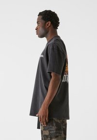 Sort bomulds oversized t-shirt med korte ærmer, som har et grafisk print på ryggen. Stoffet har en let slidt tekstur.