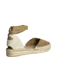 Sandalia espadrille de ante marrón con suela de yute trenzado, que presenta una correa de tela beige en el tobillo y lados abiertos, mostrando un acabado texturizado.