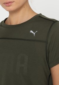 Olivgrön sporttröja tillverkad av andningsbart material. Har rundad halsringning, korta ärmar och en vit Puma-logotyp på bröstet.