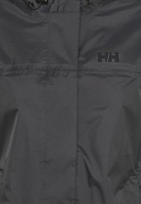 Chaqueta negra impermeable con una textura suave, presenta un cuello con cremallera y un logo en el pecho. Material ligero y durable.