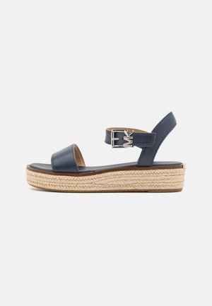 Sandalo con plateau in pelle blu navy con suola in juta intrecciata, cinturino alla caviglia con fibbia argento e logo "MK" su sfondo bianco.