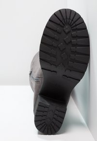 Graue Wildlederstiefel mit einer strukturierten schwarzen Gummisohle, die ein Profilmuster für besseren Halt aufweist. Details mit seitlichem Reißverschluss am Obermaterial.