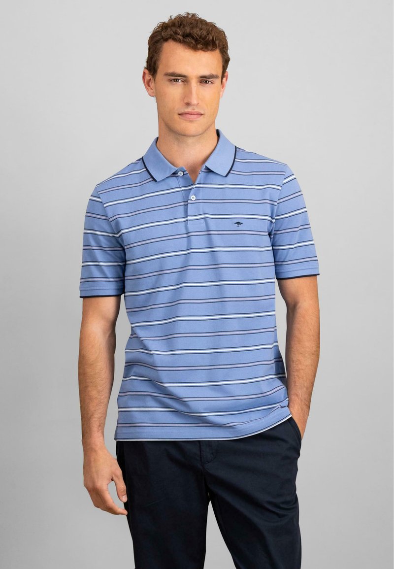 Világoskék pólóing, vízszintes sötétkék és fehér csíkokkal, rövid ujjú, klasszikus gallérral, amelyen egy kis embléma található a mellrészen.