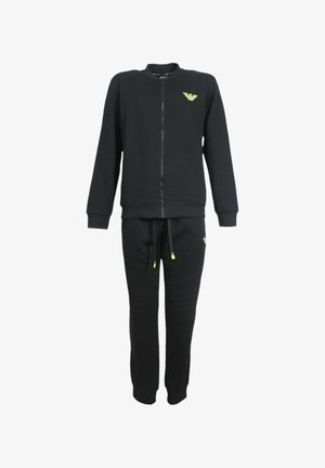 Felpa nera con zip e girocollo, decorata con un logo giallo, abbinata a pantaloni neri coordinati con lacci per regolare la vita.