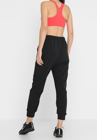 Černé joggingové kalhoty s elastickými manžetami a pasem, kombinované s korálovým sportovním crop topem. Outfit je doplněn černými sportovními botami.