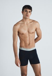 Fekete férfi boxer alsónadrág szürke derékpánttal, amelyen a "Calvin Klein" felirat található. Az anyag rugalmasnak és simának tűnik, testhezálló kialakítással.