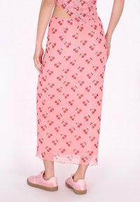Rosa maxi rok met kersenprint, doorzichtige textuur, gegolfde zoom en zijsplit, gecombineerd met roze sneakers.