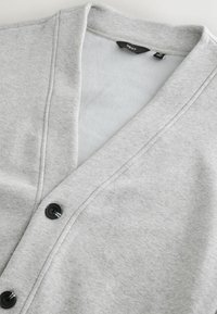 Light gray cardigan made from soft fabric with a V-neck, featuring black buttons and a smooth texture, suitable for layering.