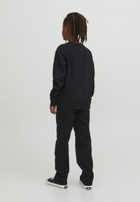Felpa nera in pile con collo rotondo, polsini a coste e pantaloni abbinati neri a vestibilità ampia con tasche laterali e sneaker classiche.