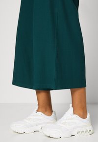 Robe midi verte à côtes et baskets Nike blanches avec des accents en maille et une semelle rembourrée visible, affichant un look sportif et confortable.