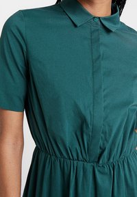 Abito camicia verde acqua con colletto, maniche corte, apertura frontale con bottoni e vita elasticizzata con dettagli arricciati.