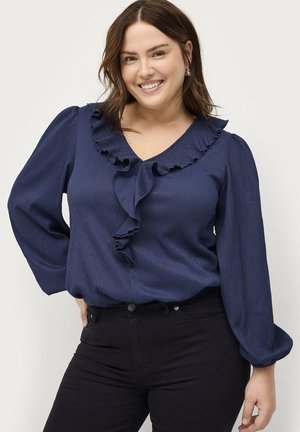 Navy blue blouse with ruffled V-neckline and long puff sleeves, made from textured fabric, paired with black jeans.
