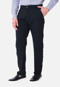 Chino in cotone navy con vestibilità dritta, dotati di tasche laterali, chiusura a bottone e indossati con scarpe nere senza lacci. Maglietta a righe visibile.