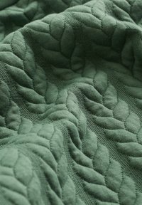 Strukturiertes grünes Stoffmaterial mit einem gesteppte, blattähnlichen Muster, das weiches, gewebtes Material in satten Grüntönen zeigt.