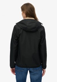 Zwarte waterdichte jas met capuchon, elastische zoom en contrasterende beige kraag. Kenmerkt zich door een gladde textuur en eenvoudig ontwerp.