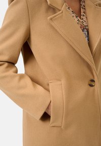Beige wollen-blend jas met een visgraattextuur, voorzien van een geknipt revers, een enkele knoopsluiting en een voorzak.