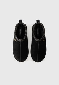 Zwarte suède pantoffels met een getextureerde zwarte voering, een schuine lijn, en gouden branding, met een subtiele naaddetail aan de voorkant.
