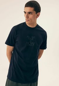 Granatowa bawełniana koszulka z krótkim rękawem i okrągłym dekoltem. Posiada biały tekst, który brzmi: „WSZYSTKO, CO MAMY, TO TERAZ HENDERSON CO.”