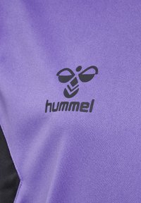 Lila träningsskjorta med svarta detaljer, med en svart logotyp av en stiliserad bi och varumärkesnamnet "hummel" tydligt synligt.