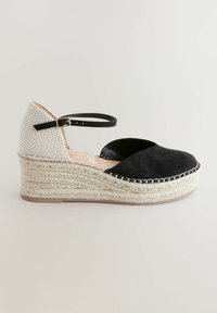 Espadril din suede negru cu toc wedge, cu o partea superioară țesută alb-negru, curea de gleznă și talpă intermediară din jută împletită. Talpă exterioară din cauciuc plat.
