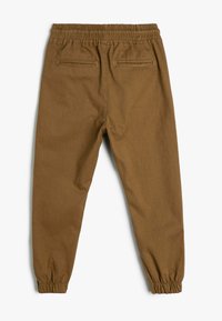 Brune bomuldsbukser med elastisk talje, slim fit, elastiske stropper ved anklerne og to baglommer. Glat tekstur med en mat finish.