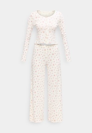 Witte geribbelde top met lange mouwen en bijpassende wijde pijpen broek met een klein roze bloemmotief en gegolfde randen.