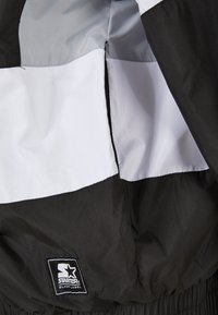 Jachetă bicicleta alb-negru cu textură netedă, având un tag de logo proeminent și panouri de culoare contrastantă pe interior.