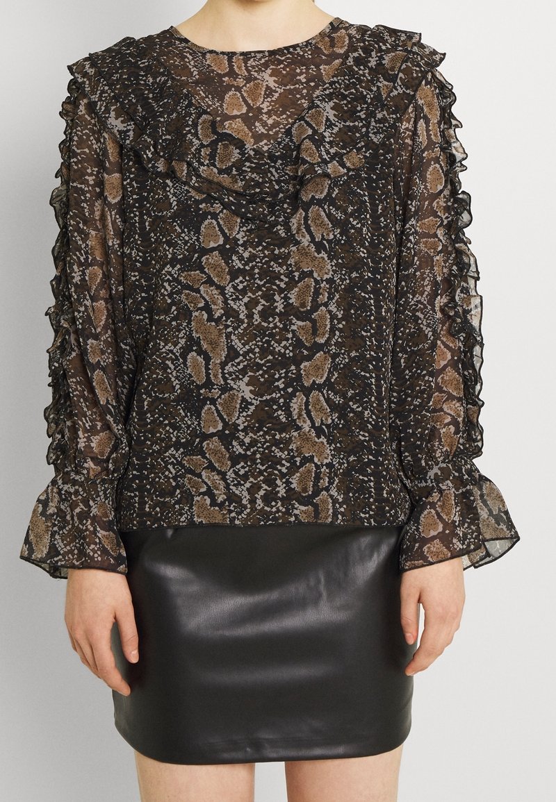 Blouse noire transparente avec imprimé serpent, col et manches à volants. Associée à une mini-jupe noire en cuir ajustée.