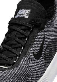 Czarno-szary sneaker Nike Free z plecioną teksturą, płaskimi czarnymi sznurowadłami, wyściełanym kołnierzem oraz czarnym logo Swoosh po boku.
