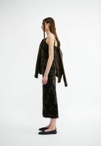 Schwarzes, mit Blumenmuster versehenes Samtkleid mit Spitzenbesatz, kombiniert mit einer braunen Lederjacke, die über eine Schulter drapiert ist, und schwarzen Ballerinas.