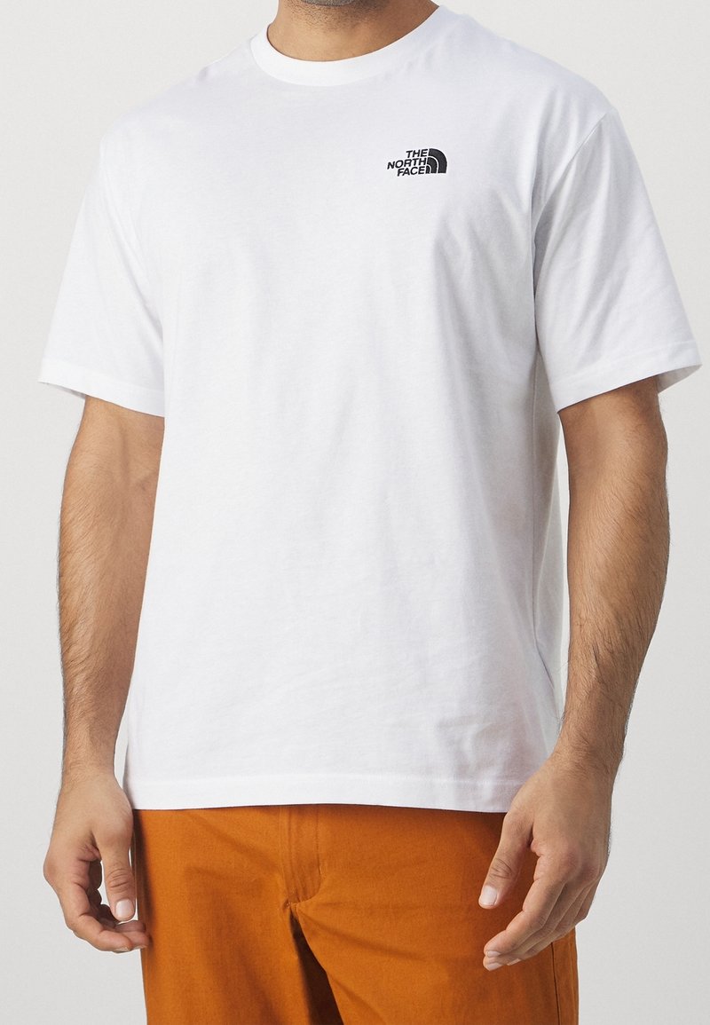 Camiseta blanca de algodón con mangas cortas que presenta un pequeño logo negro en el lado izquierdo del pecho. Hemo recto, ajuste casual y textura suave.