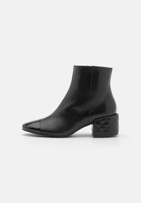 Sorte skinn ankelboot med spiss tå, blankhette og kviltet blokkhæl-design. Glatt tekstur med en slank silhuett.