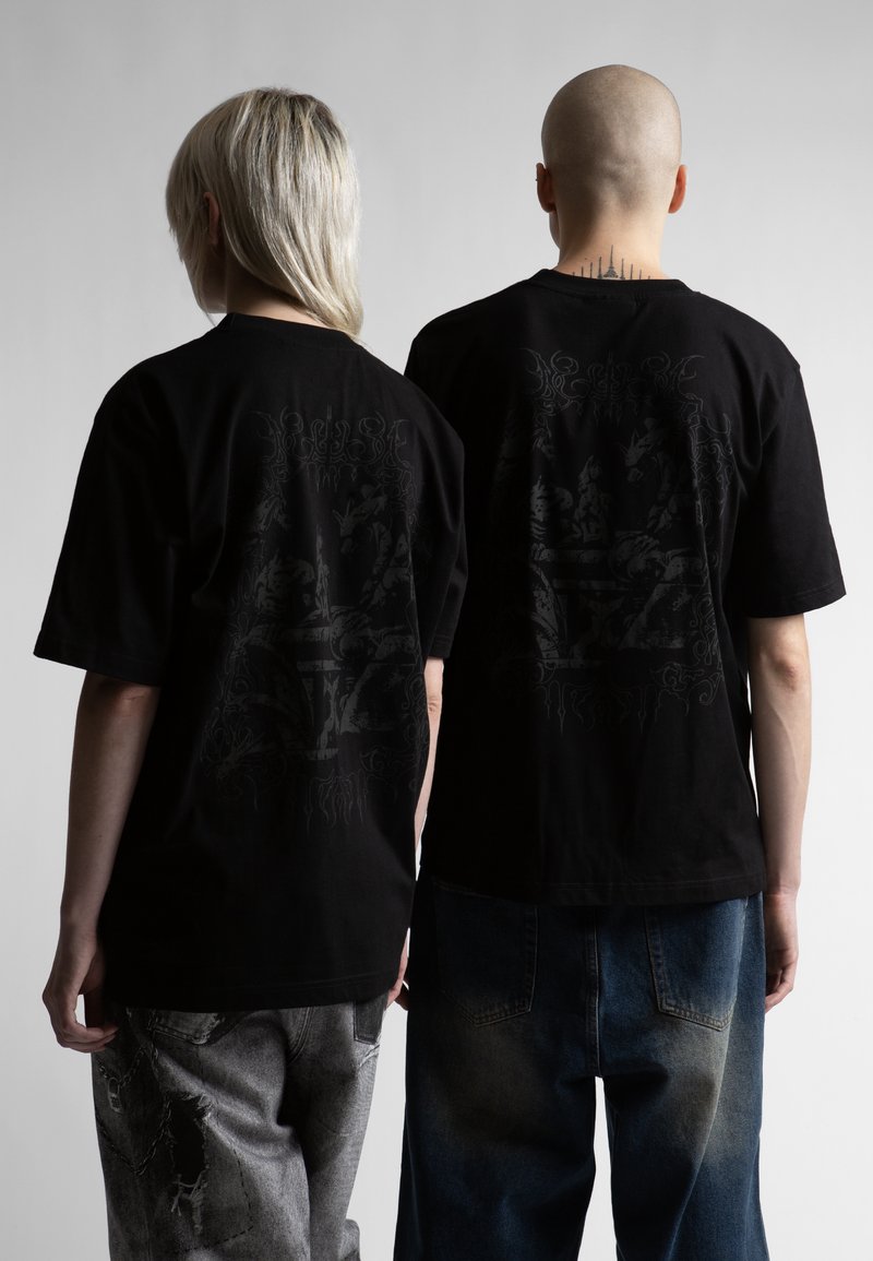 Δύο άτομα που κοιτούν προς τα πίσω φορούν μαύρα γραφικά μπλουζάκια. Το ένα έχει μακριά ξανθά μαλλιά και κονδυλώδη γκρι τζιν, το άλλο είναι φαλακρό με μπλε τζιν.