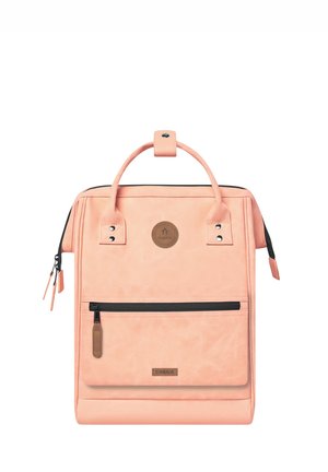 Peach-colored backpack made of soft material features a top handle, front zipper pocket, and a logo patch. Includes accent hardware details.