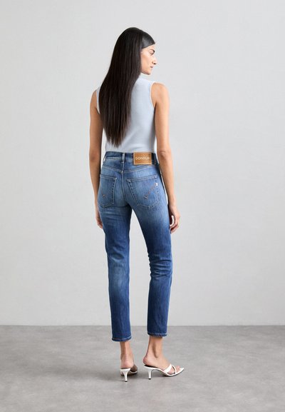 Jeans de mezclilla azul de cintura alta con un ajuste slim, ligero desgastado, bolsillos traseros y una etiqueta de cuero de la marca. Combinados con una camiseta sin mangas de canalé gris.