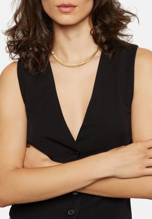 Schwarzes ärmelloses Kleidungsstück mit tiefem V-Ausschnitt und Knopfdetails. Eine goldene Halskette mit einem strukturierten, geschwungenen Design liegt am Ausschnitt.