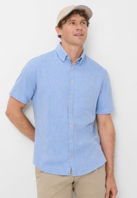 Lichtblauw kortekleurig overhemd met knopen en een pockets, gemaakt van een structuurtstof. Gestyled met een beige pet met een gebogen rand.
