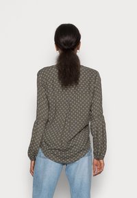 Chemise boutonnée vert olive avec petits motifs floraux blancs et bleus. Manches longues, ourlet arrondi et détail en tissu doux au dos.