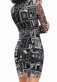 Robe moulante noire et blanche avec un motif graphique imprimé de lettres et de chiffres. Manches longues et silhouette ajustée. Texture transparente.