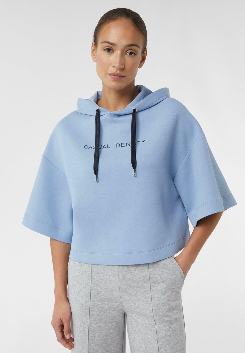 Cappuccio corto di colore blu chiaro realizzato in tessuto morbido, con una grafica frontale "CASUAL IDENTITY" e lacci neri, abbinato a pantaloni della tuta grigi.