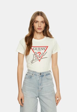 T-shirt bianco in cotone con un logo triangolare rosso, testo "GUESS U.S.A." e decorazioni argentate che formano la parola "Love." Abbinato a jeans in denim chiaro.