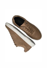 Baskets en cuir marron avec une surface texturée, bout rond et semelle en caoutchouc blanc ; elles présentent un design à lacets et des coutures décoratives.