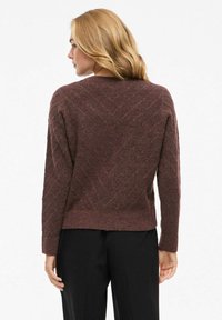 Mauve stickad tröja med ett strukturerat zigzag-mönster, långa ärmar och rundad halsringning, i kombination med svarta byxor.