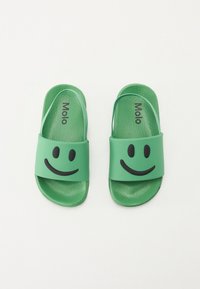 Grønne sklidesandaler med en struktureret overflade, der har et fremtrædende sort smilende ansigt design på remmen samt "Molo" branding.