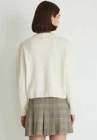Cream-colored, textured sweater with a cropped fit, ribbed hem, and long sleeves, paired with a plaid pleated skirt in earthy tones.