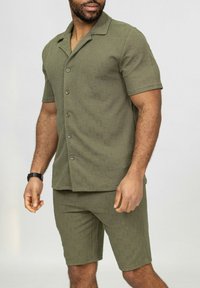 Chemise à manches courtes olive avec un short assorti en tissu texturé, comportant un col et des boutons sur la chemise, et une coupe à l'intérieur de la jambe sur le short.