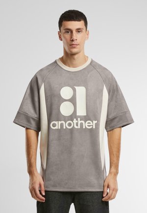 T-shirt supradimensionat gri cu mâneci scurte, accente crem și un imprimeu grafic mare care spune "another" într-o culoare contrastantă. Textură moale.