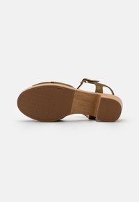 Sandale marron avec une semelle en caoutchouc texturé, un talon en bois, des brides vert olive et une fermeture à boucle. Design ouvert au niveau des orteils avec des caractéristiques minimalistes.